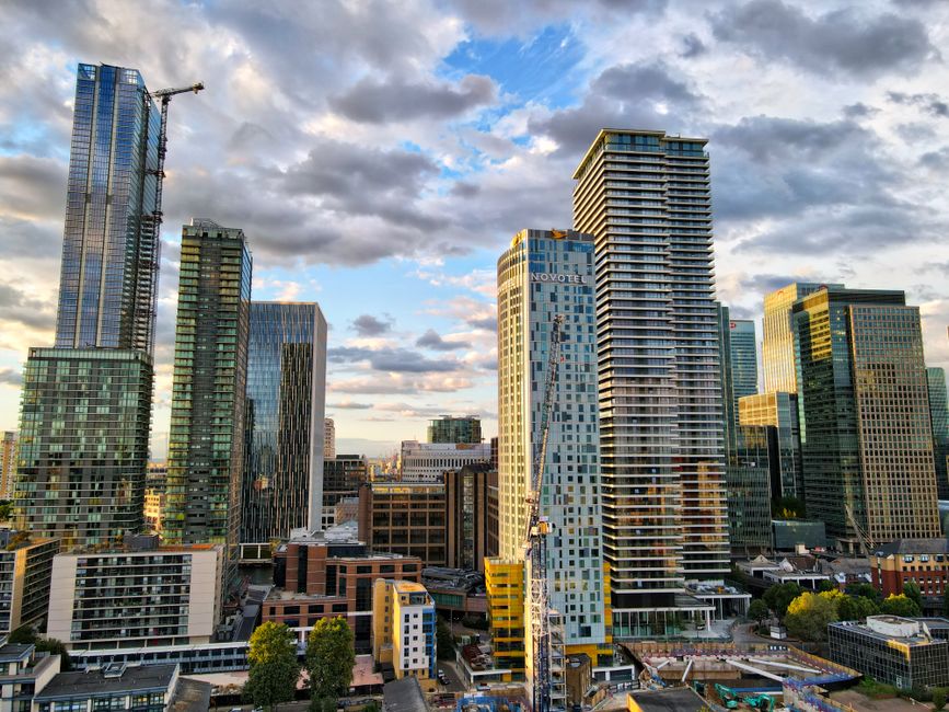 A high-angle view of a modern city skyline in London, featuring tall glass office buildings with reflective surfaces and contemporary architectural designs. The scene is illuminated by natural dayligh